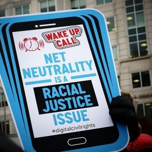 sign held by a gloved hand reading Net Neutrality is a racial justice issue #digitalcivilrights